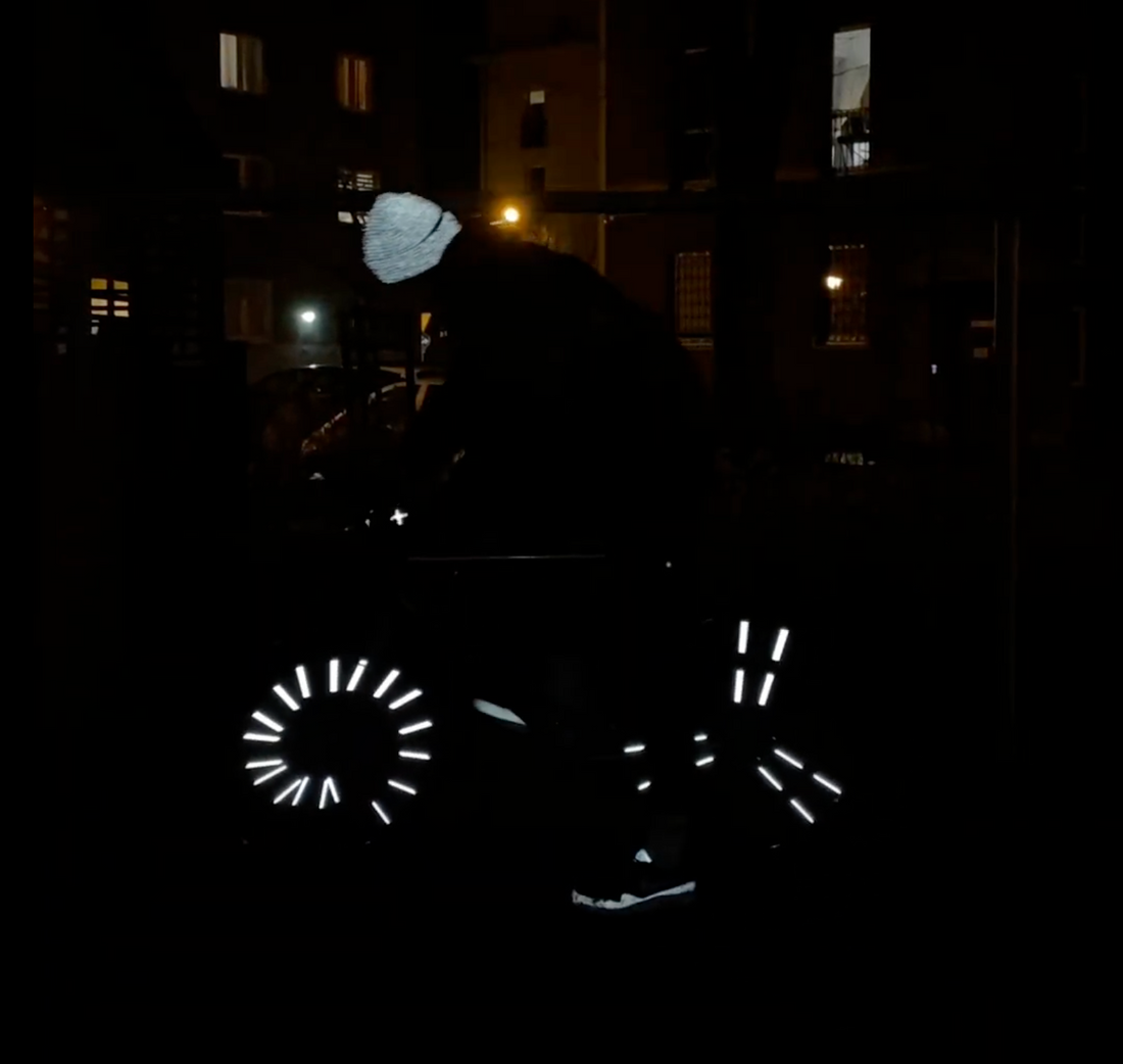 Radfahrer bei Nacht mit leuchtenden Flex Clips, reflektierender Flex Mütze und reflektierenden Handschuhen in urbaner Umgebung.