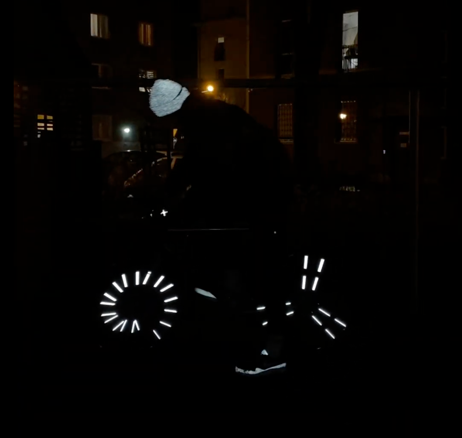 Radfahrer bei Nacht mit leuchtenden Flex Clips, reflektierender Flex Mütze und reflektierenden Handschuhen in urbaner Umgebung.